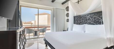 A bedroom with a large bed, a TV, and a balcony with a chair.