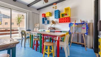 Children can play and explore in this vibrant playroom with a large window offering a view of the outside, a wooden table, colorful chairs, and a toy piano.