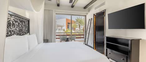 A hotel room with a large bed, a ceiling fan, a TV, and a balcony with outdoor seating.