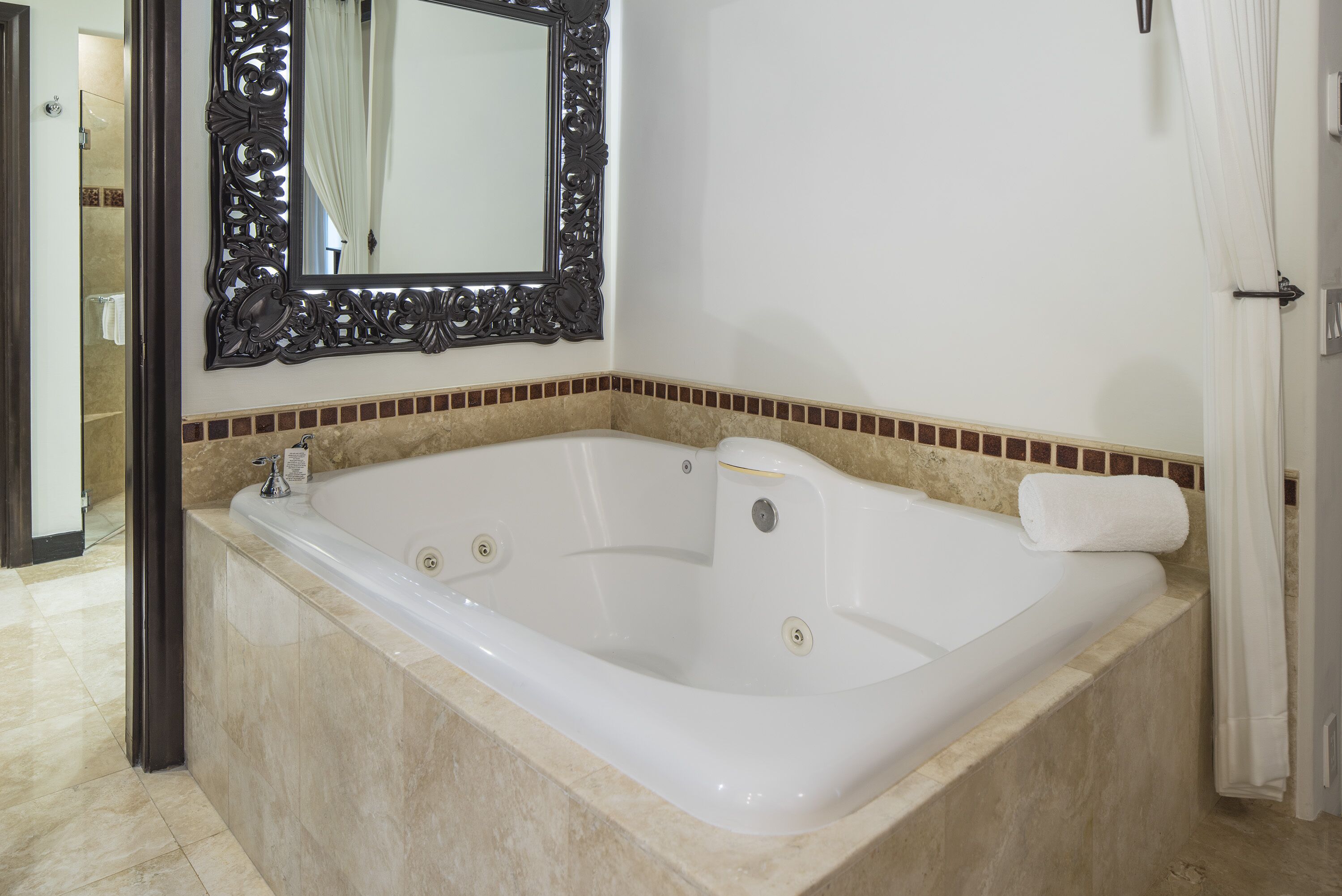 A large, rectangular bathtub with a single faucet, a decorative mirror above it, and a towel on the edge.