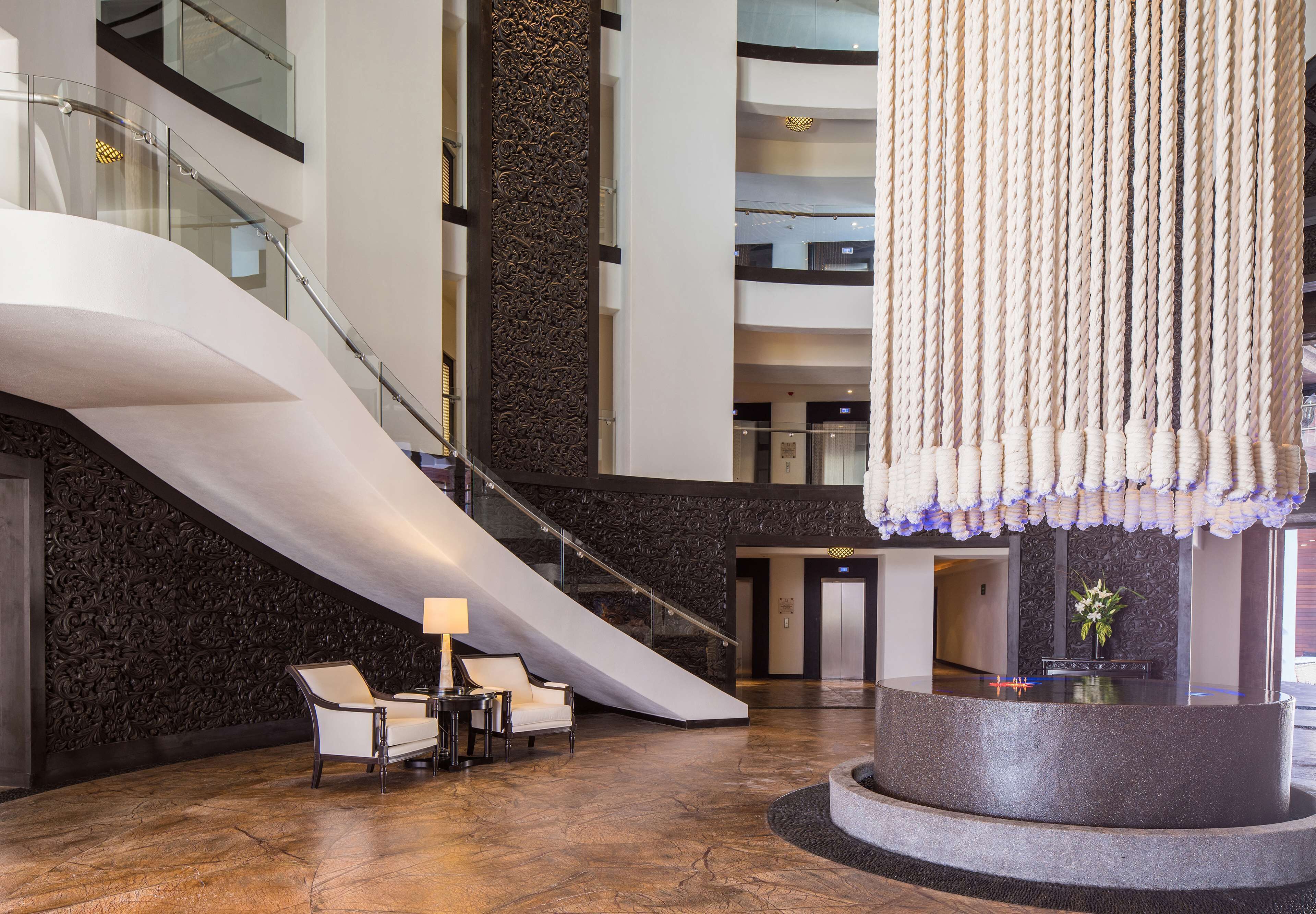 A modern lobby with a central staircase, seating area, and a reception desk.