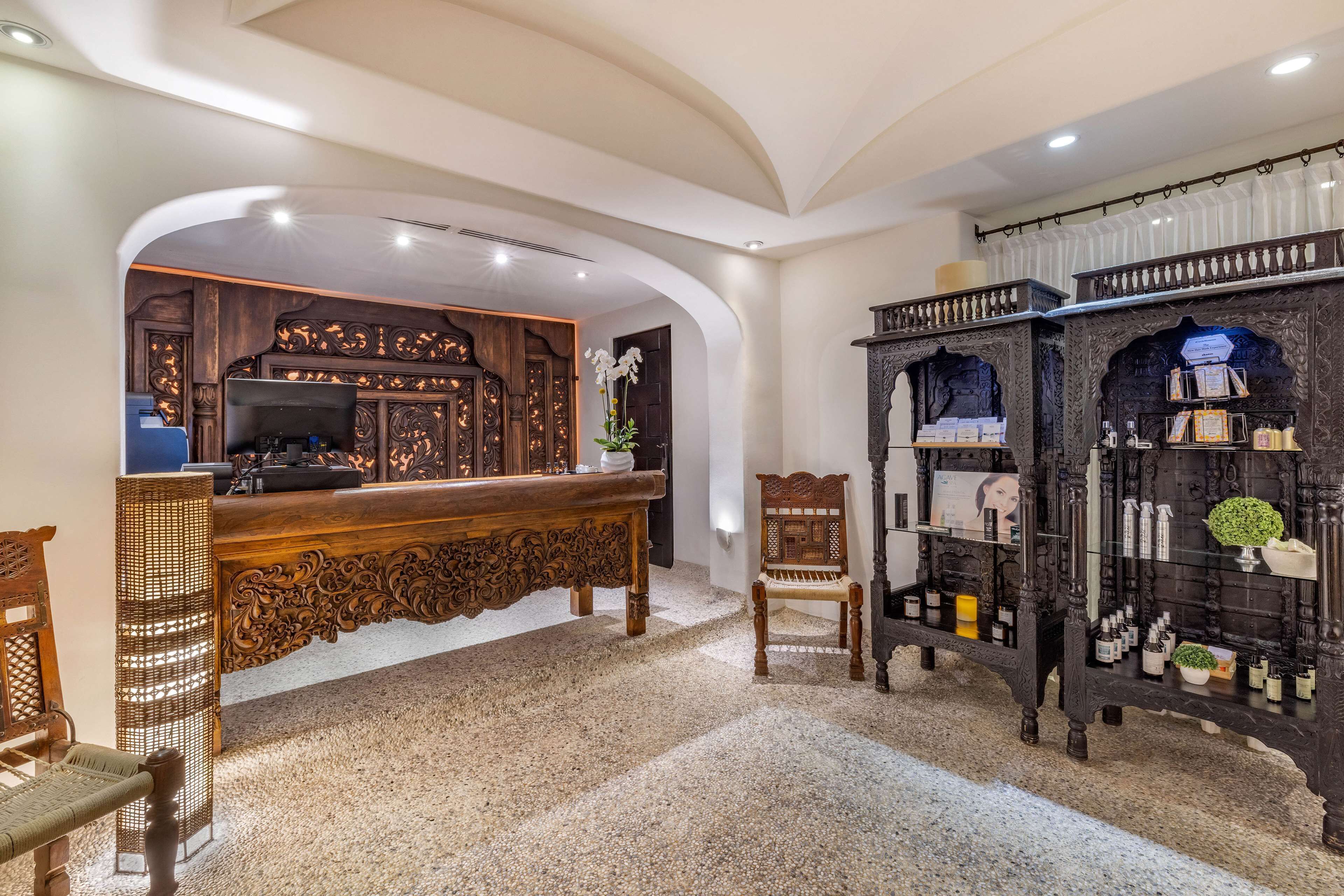 A reception area with a wooden reception desk, a chair, a shelf with toiletries, and a decorative wall with intricate carvings.