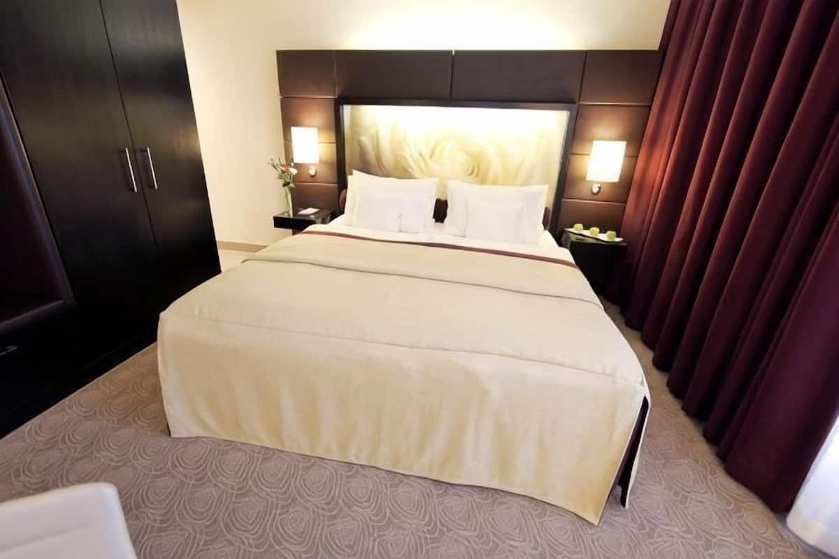 Una habitación de hotel con una cama grande, cabecera oscura, lámparas de noche y una mesita.