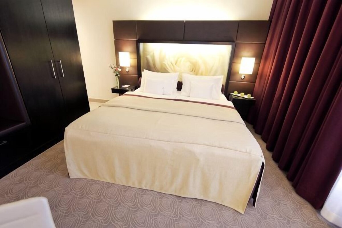 A hotel room with a large bed, dark headboard, bedside lamps, and a nightstand.