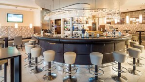 A bar area with a curved counter, multiple stools, and a variety of bottles and glasses. - Lindner Hotel Vienna Am Belvedere, part of JdV by Hyatt (Vienna)