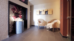 A modern lobby with a tiled floor, a decorative wall with a floral painting, a blue vase with flowers, two wicker chairs, and a shelf with towels. - Lindner Hotel Vienna Am Belvedere, part of JdV by Hyatt (Vienna)