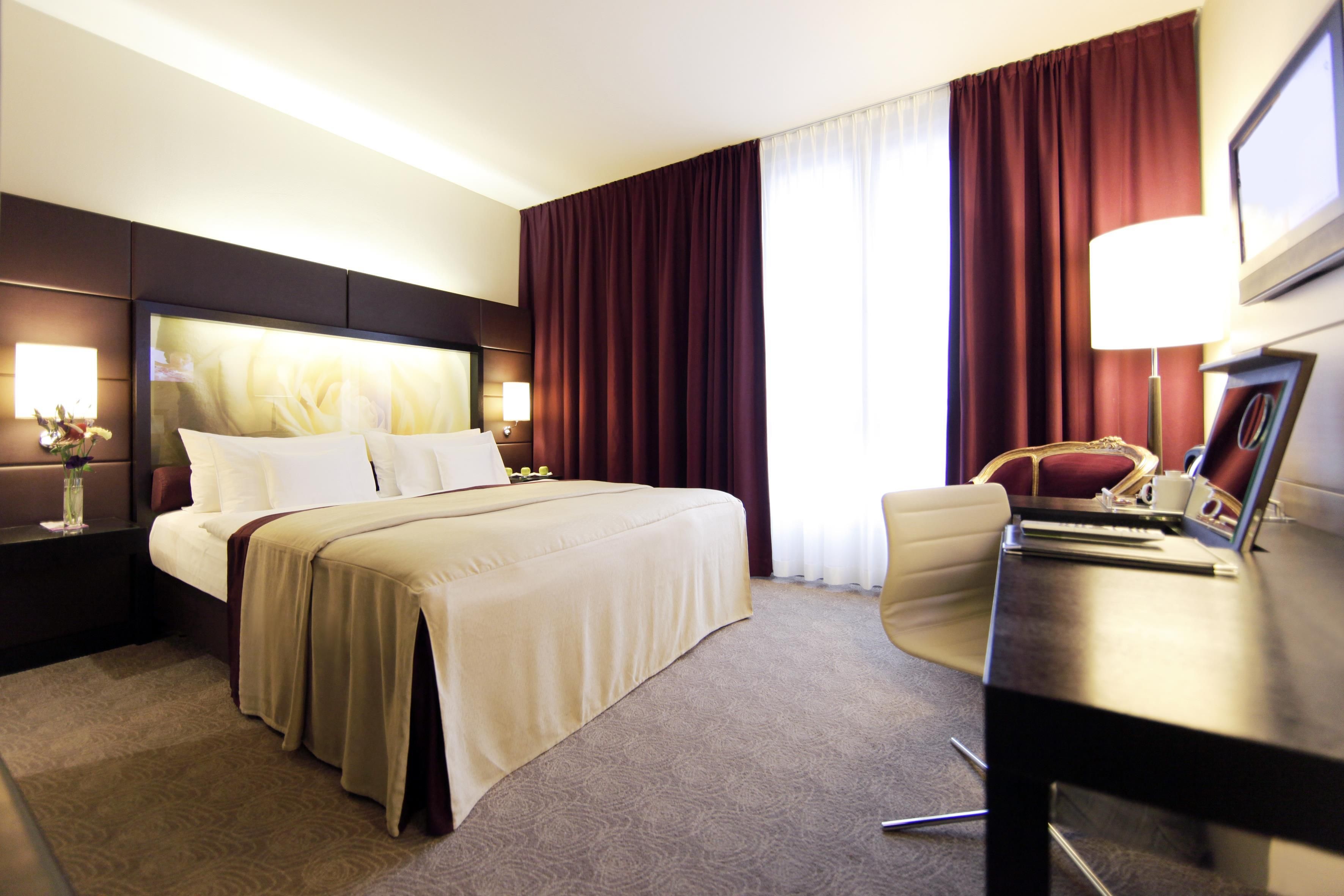 A hotel room with a large bed, a desk, a chair, and a window with curtains.