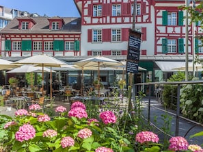 A restaurant with outdoor seating, red and white facades, and a signboard with text. - Hotel Hofgarten (Lucerne)