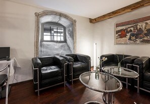 A room with a large arched window, black leather sofas, a glass coffee table, and a poster on the wall. - Hotel Hofgarten (Lucerne)