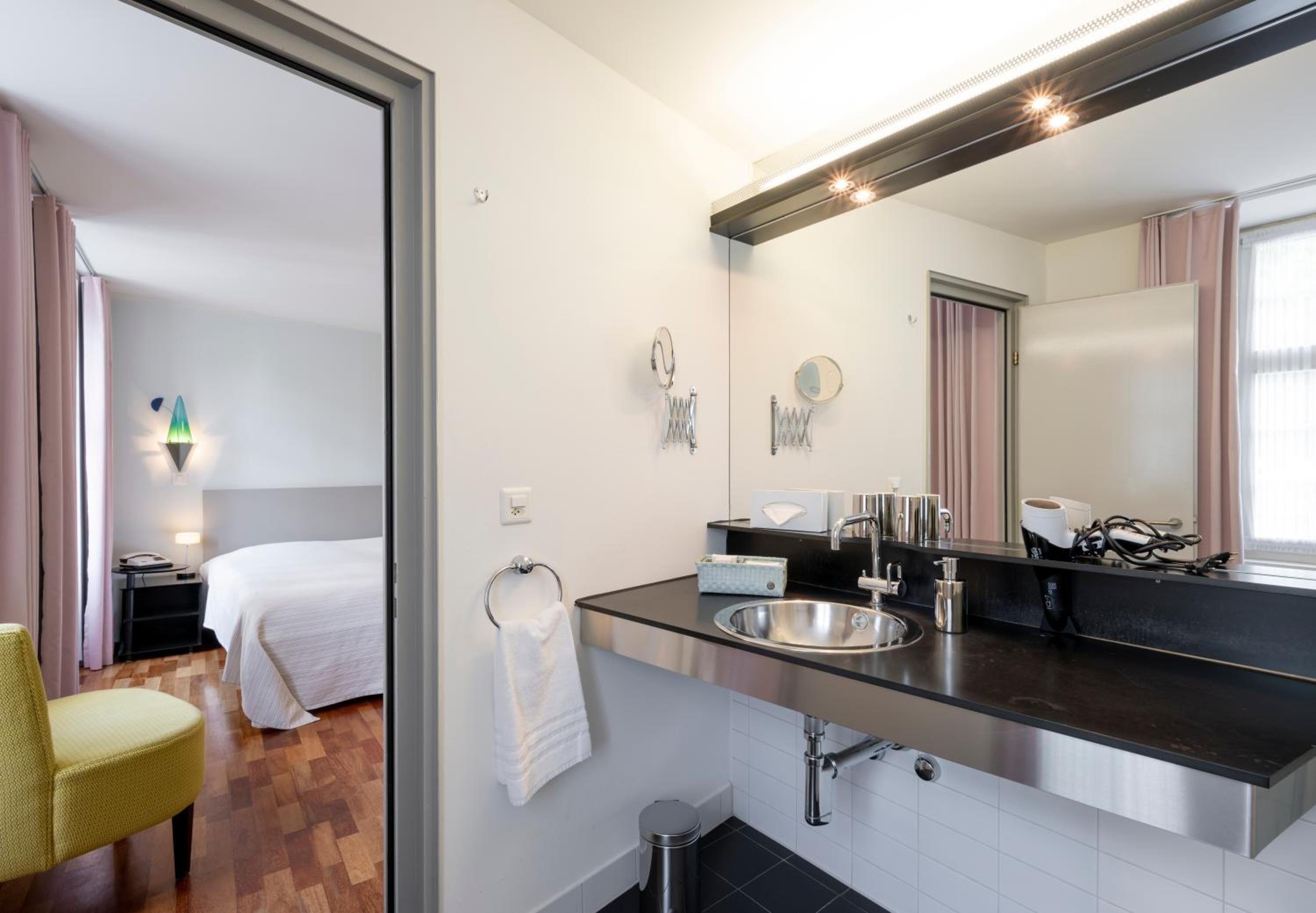 Un baño de hotel moderno con un espejo grande, un lavamanos y un inodoro.