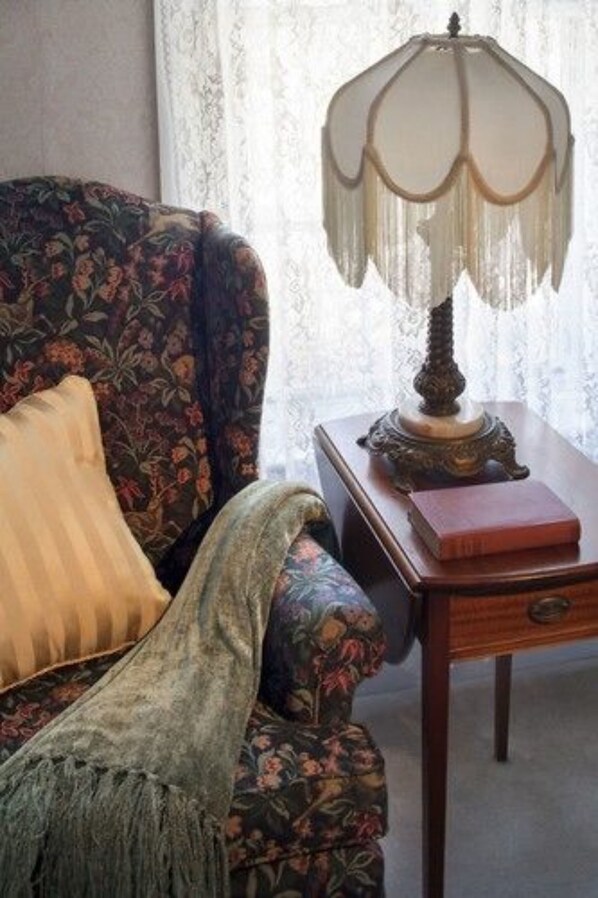 A room with a floral-patterned armchair, a fringed table lamp, and a book on a wooden side table. - Isaiah Jones Homestead Bed & Breakfast (Sandwich)