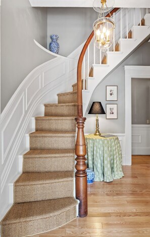 A staircase with a wooden handrail, a chandelier, and a table with a patterned tablecloth. - Isaiah Jones Homestead Bed & Breakfast (Sandwich)