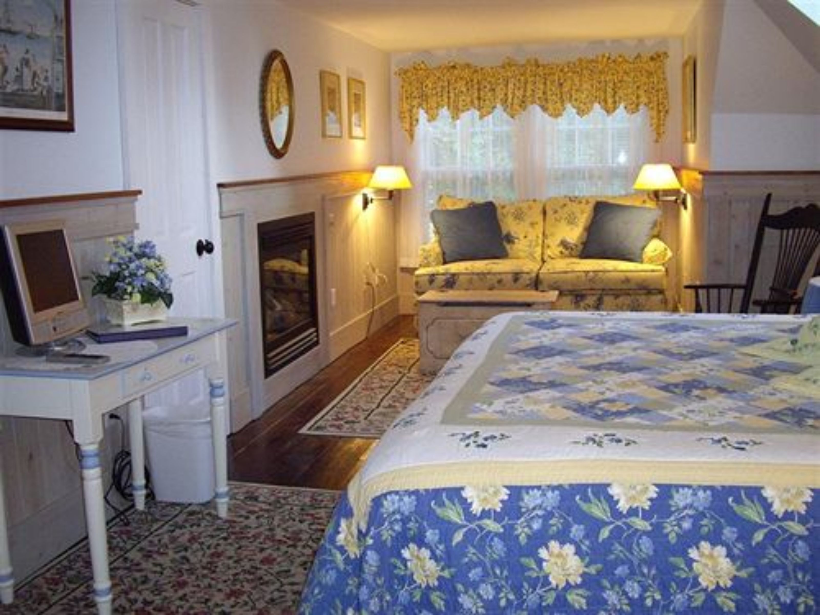 Un dormitorio con cama, escritorio con ordenador, chimenea y ventana con cortinas.