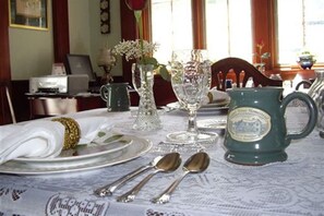 A dining table set with plates, silverware, a green mug, and a vase with flowers. - Isaiah Jones Homestead Bed & Breakfast (Sandwich)