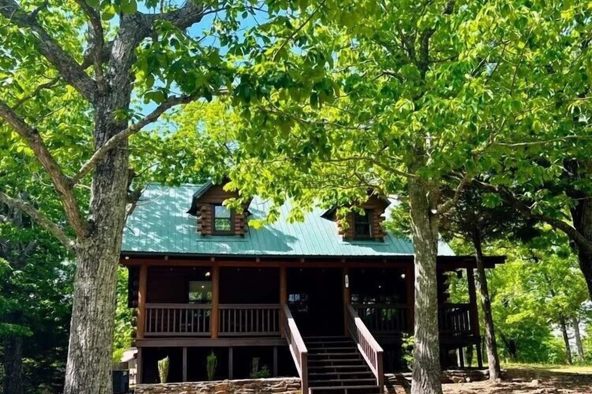 A cabin with a porch, wooden exterior, and a green roof.
