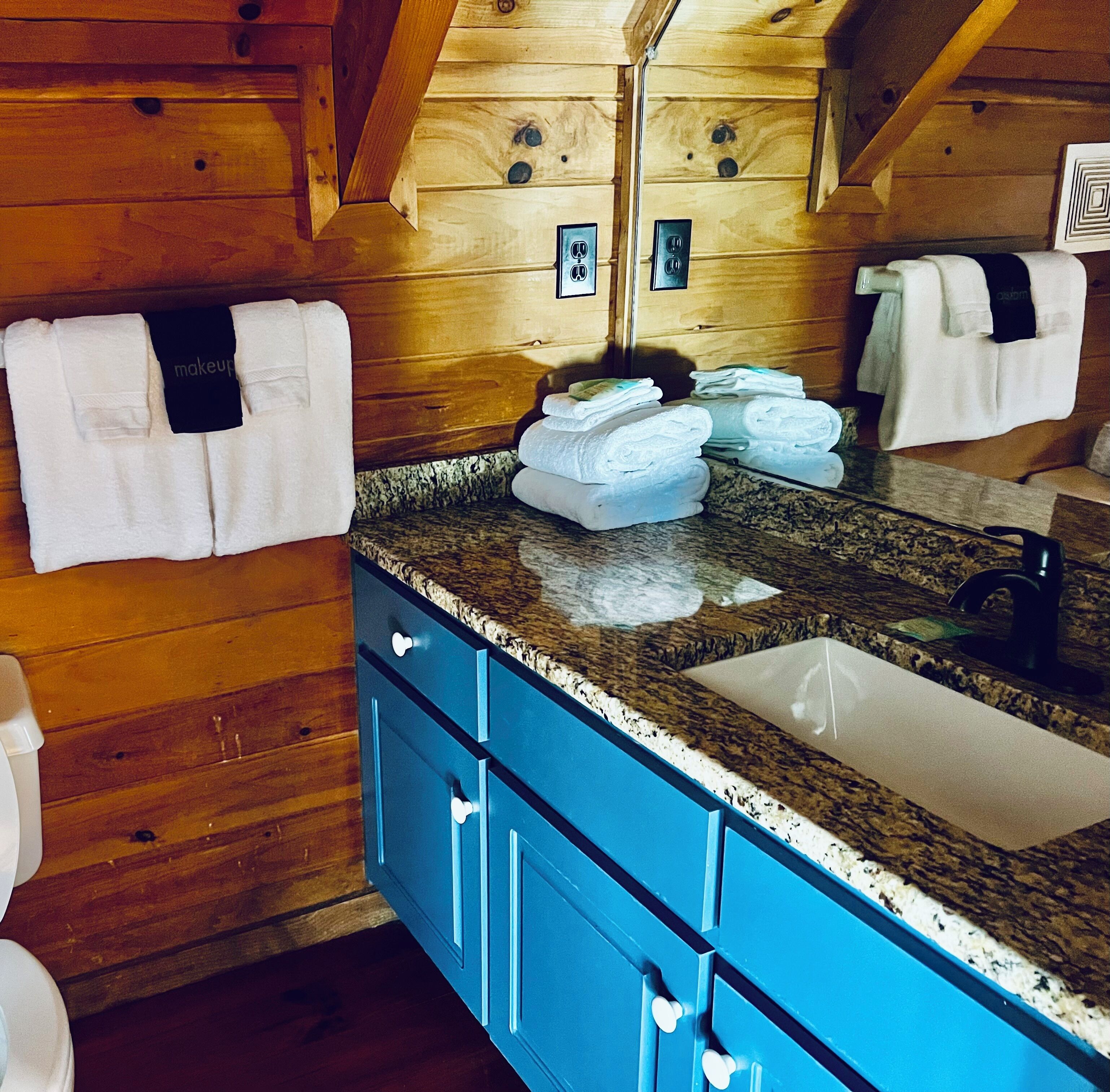 A wooden cabin interior with a bathroom featuring a granite countertop, a sink, and blue cabinets.