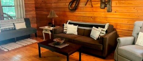 A cozy wooden cabin interior with a sofa, armchair, and a small table.