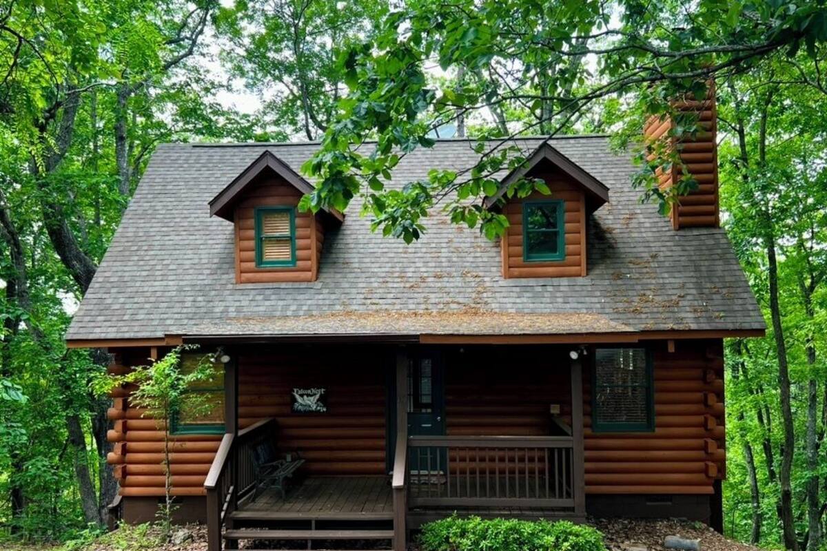 A log cabin with a porch, two windows, and a chimney.