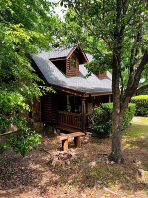 Un chalet rustique doté d’une terrasse en bois, entouré d’arbres et d’un mur de pierres.