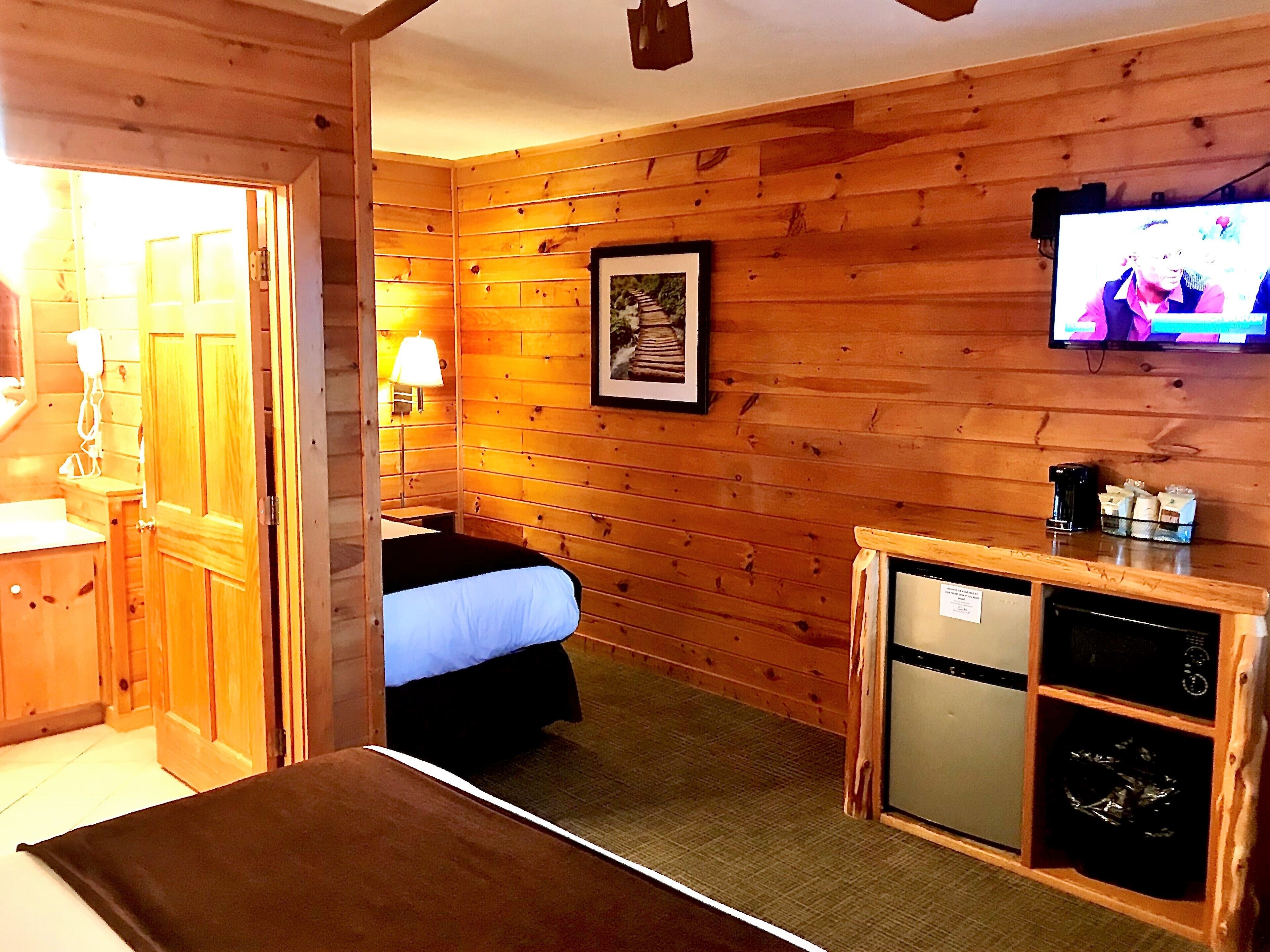 Een houten kamer met een bed, een klein bureau met een koffiezetapparaat, een aan de muur bevestigde televisie en een lijst op de muur.