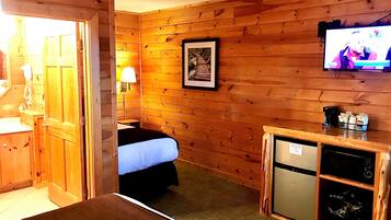 Een houten kamer met een bed, een klein bureau met een koffiezetapparaat, een aan de muur bevestigde televisie en een lijst op de muur.