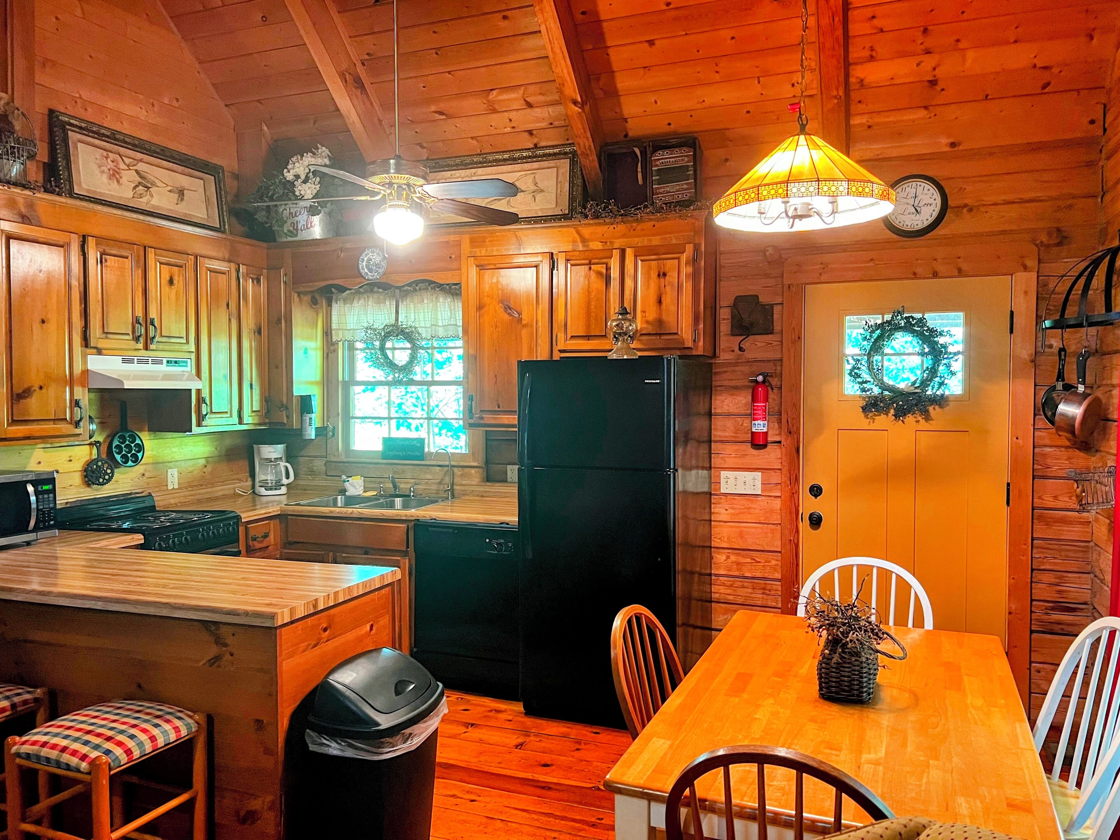 A wooden cabin-style kitchen with a dining area, wooden cabinets, a black refrigerator, and a chandelier.