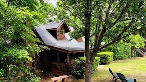 A cabin with a porch, a bench, and a tree in the foreground. - Mountain Top Inn and Resort (Warm Springs)