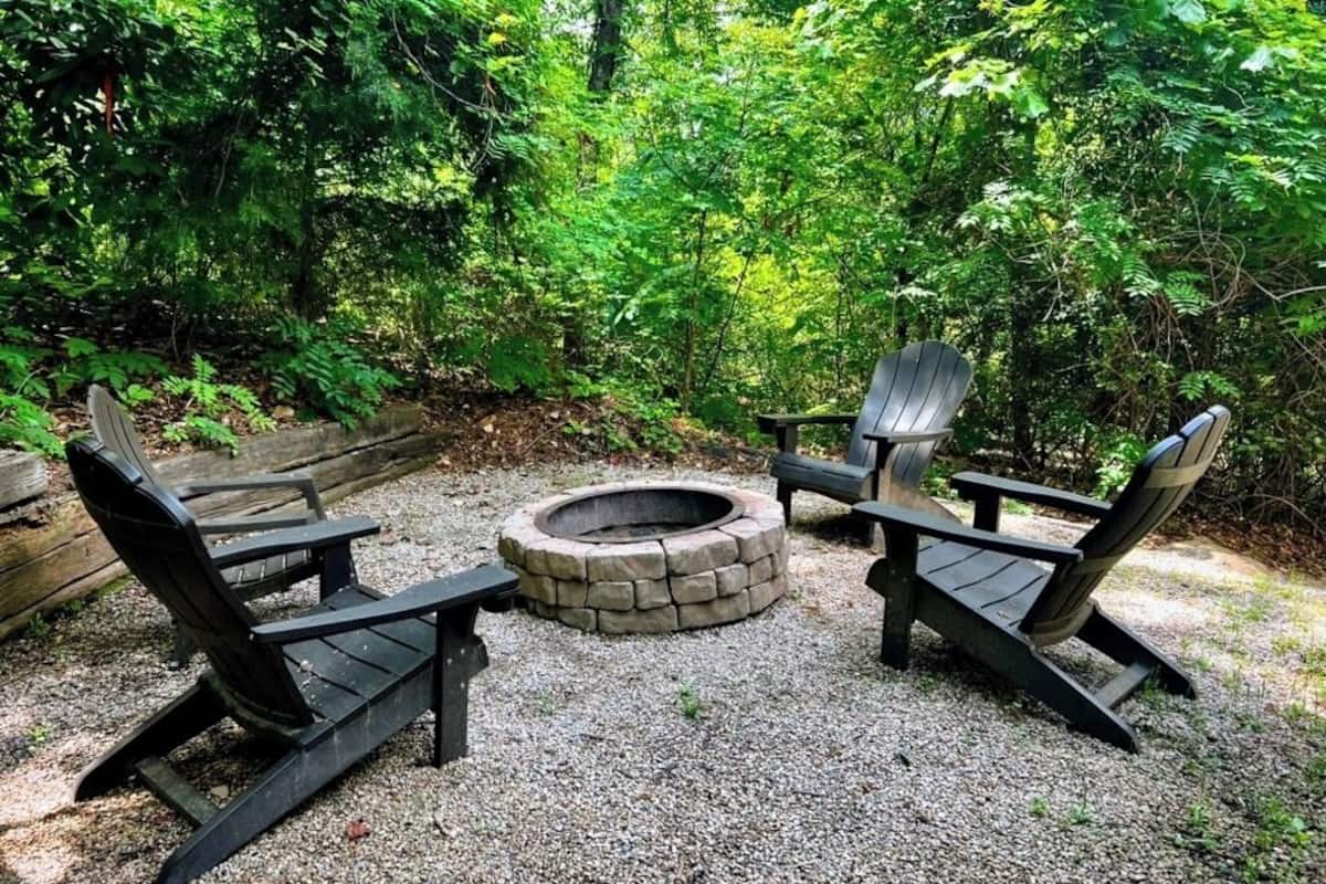 An outdoor seating area with Adirondack chairs and a stone fire pit surrounded by gravel.