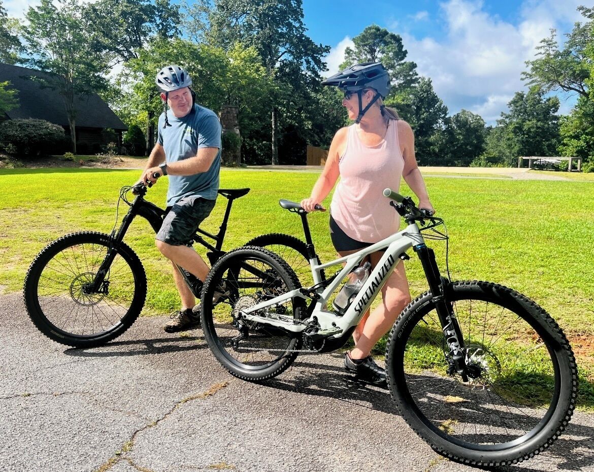 Dos bicicletas sobre un camino pavimentado, con césped y árboles al fondo.