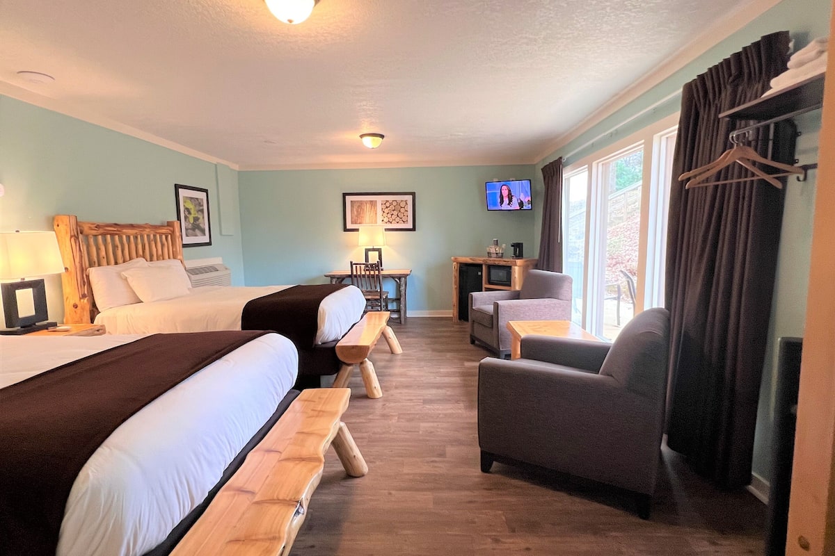 A hotel room with two beds, a desk, a chair, a TV, and a window with curtains.
