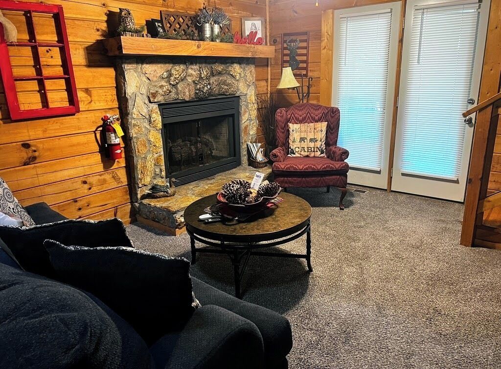 A cozy living room with a stone fireplace, a red chair, and a round coffee table.