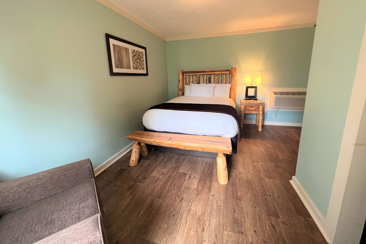 A bedroom with a wooden bed, a nightstand with a lamp, and a framed picture on the wall.