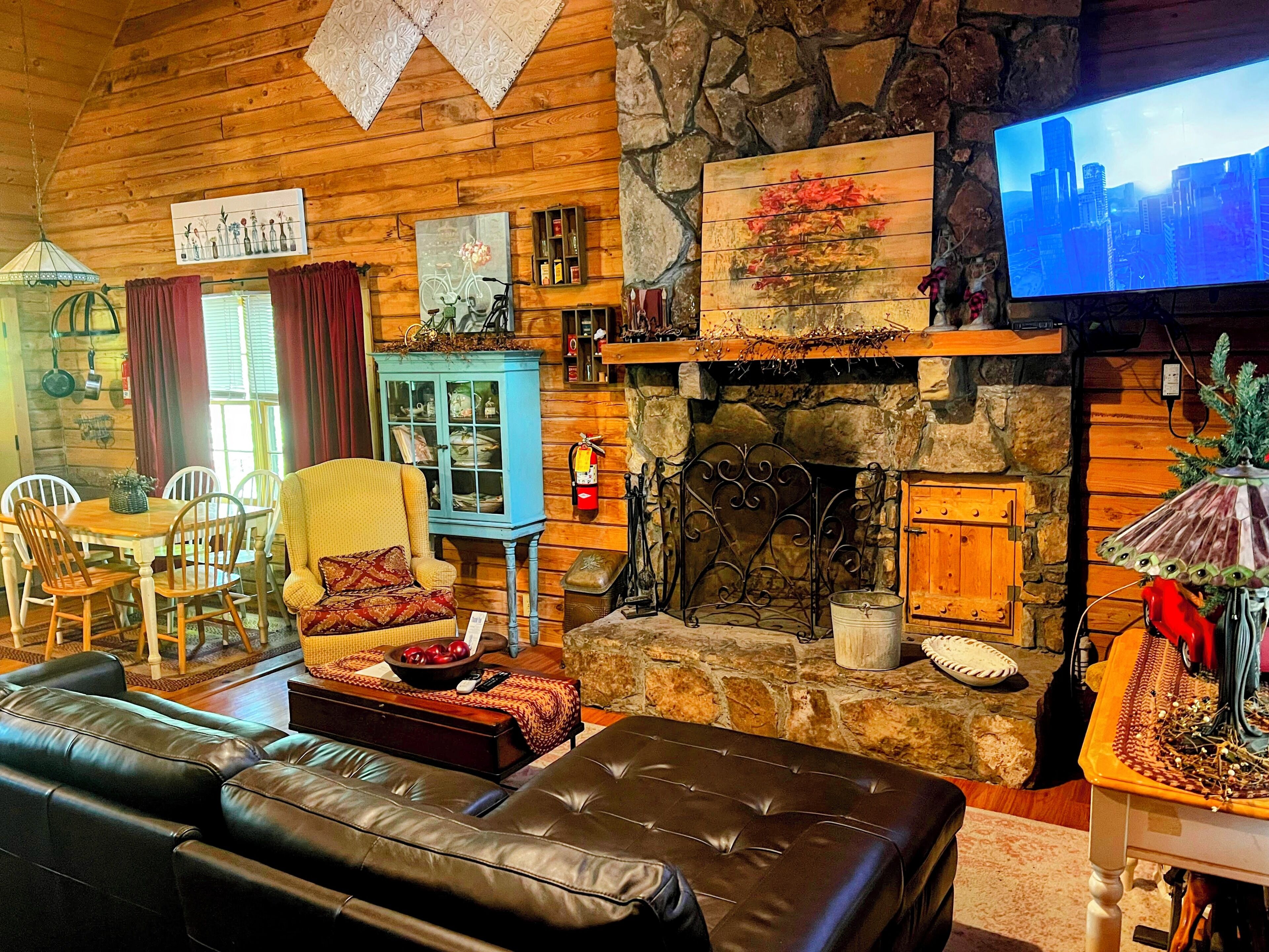 A cozy living room with a stone fireplace, a television, and a dining area with wooden furniture.