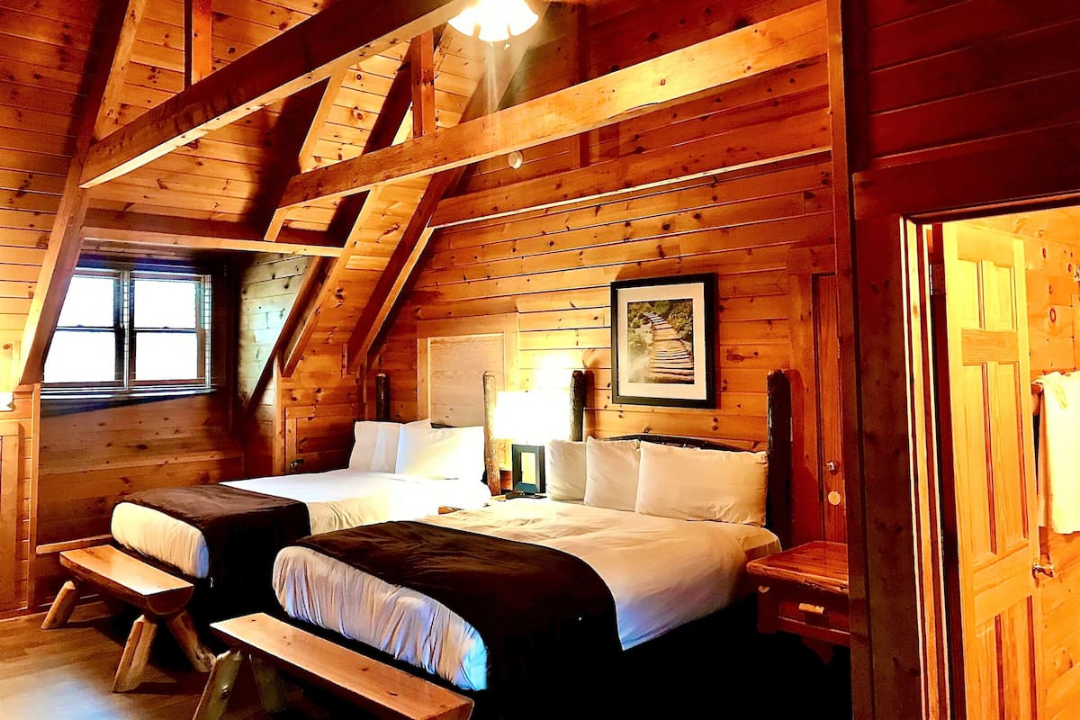 A cozy log cabin room with two beds, a bench, and a framed picture on the wall.