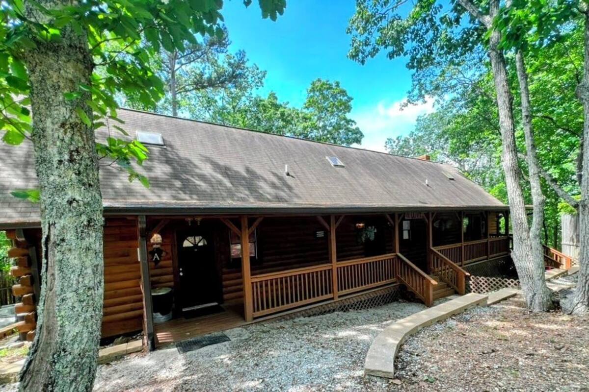 A log cabin with a porch, a covered outdoor seating area, and a gravel driveway.