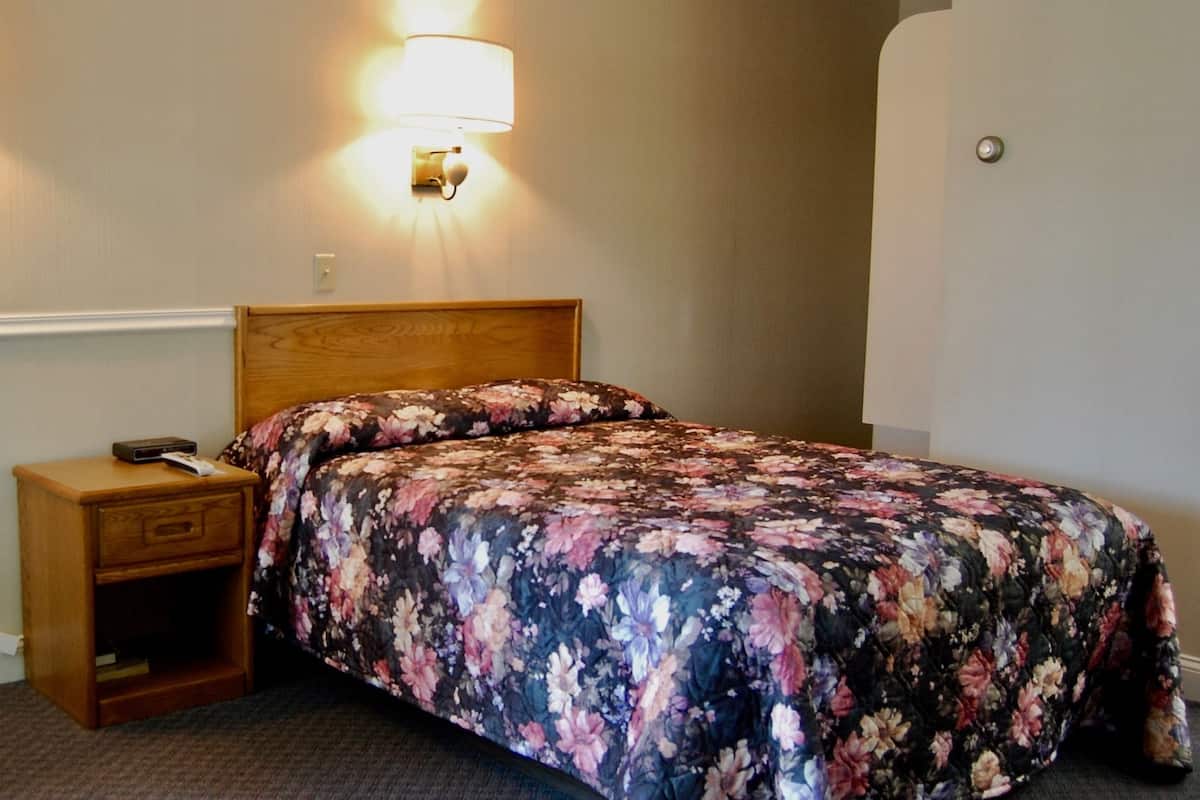 A neatly made bed with a floral bedspread, a bedside table with a lamp, and a wall-mounted light fixture.