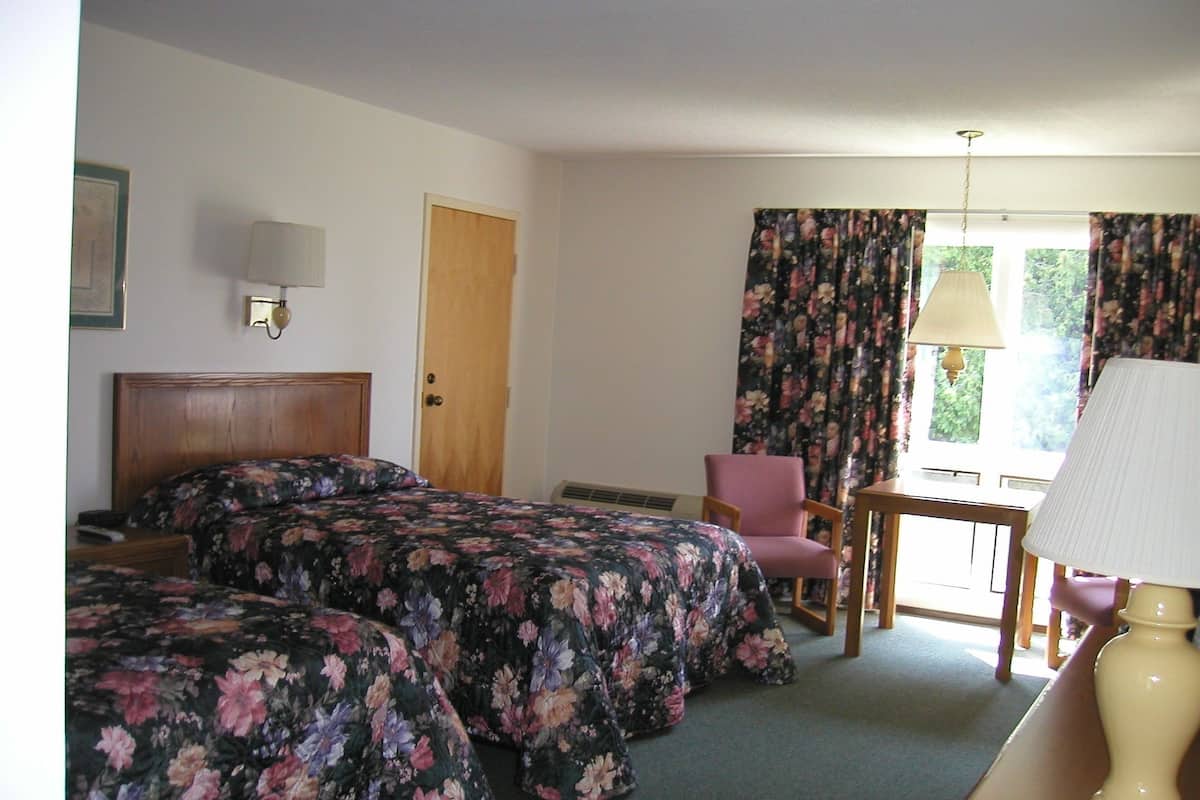 A hotel room with two beds, a chair, a table, a lamp, and a window with curtains.