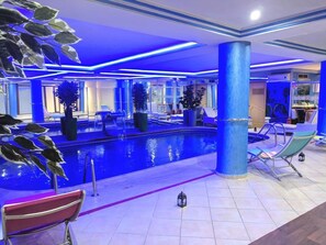 An indoor swimming pool area with blue lighting, lounge chairs, and potted plants. - Hotel Rabat (Rabat)