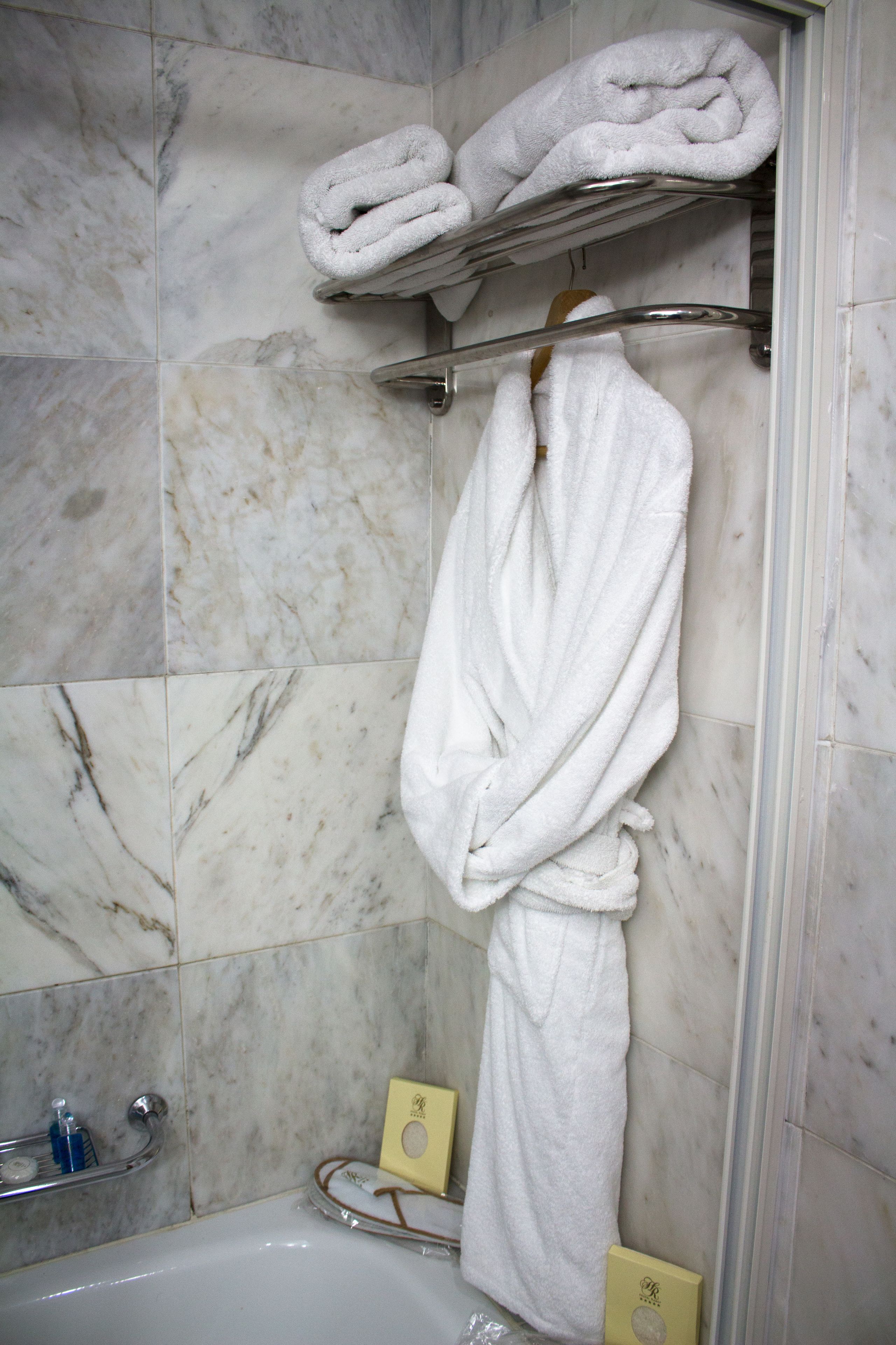 Um banheiro com parede de mármore, uma banheira e um porta-toalhas com duas toalhas dobradas.