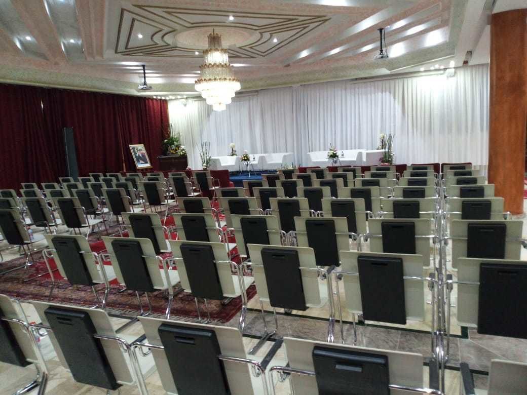 Un salón de conferencias con filas de sillas, un escenario con un atril y una araña.