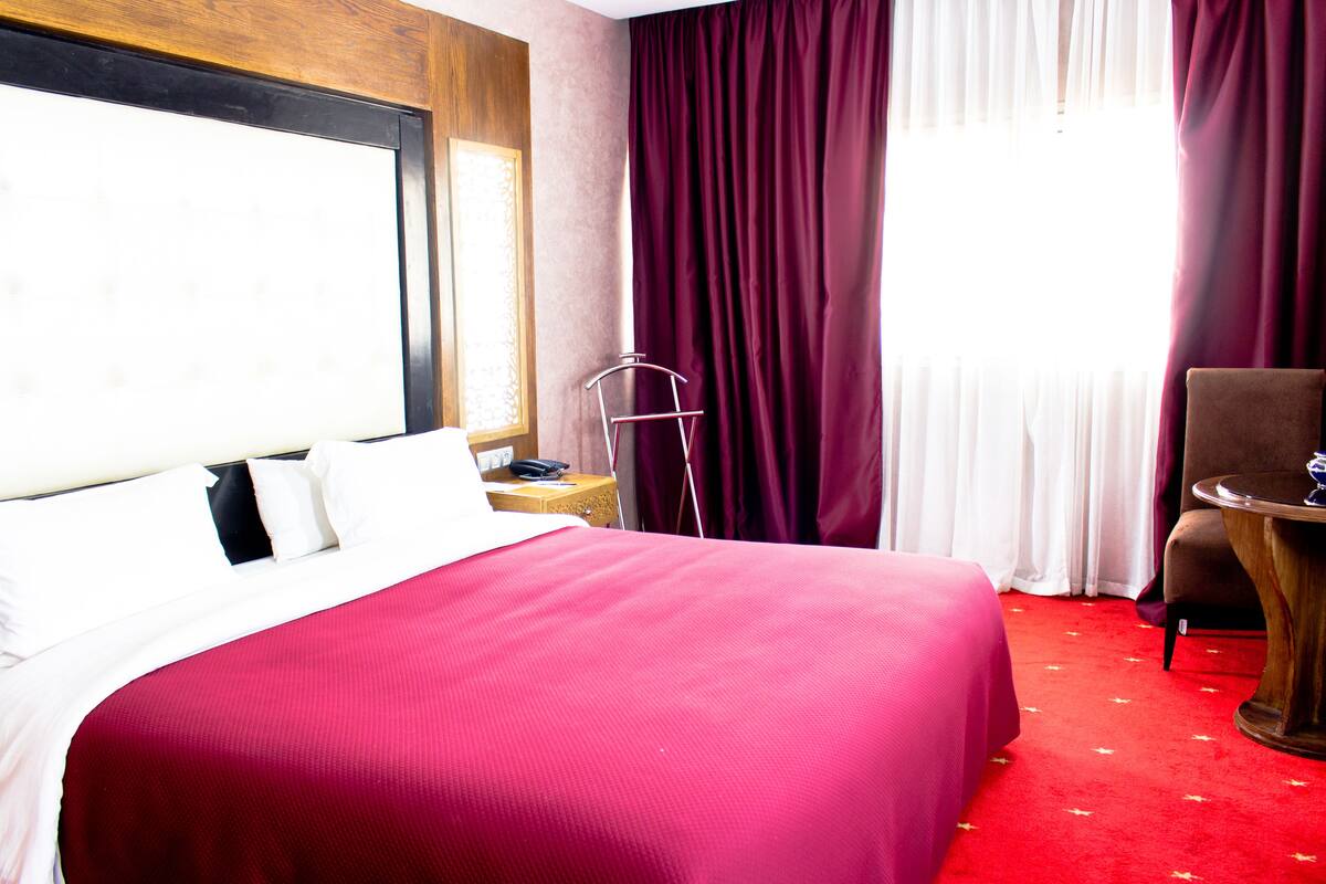 A hotel room with a large bed, a wooden headboard, a red carpet, a chair, and a small table.