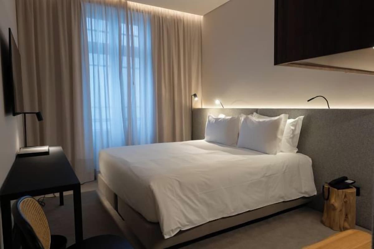 A modern hotel room with a large bed, a desk, and a TV mounted on the wall.