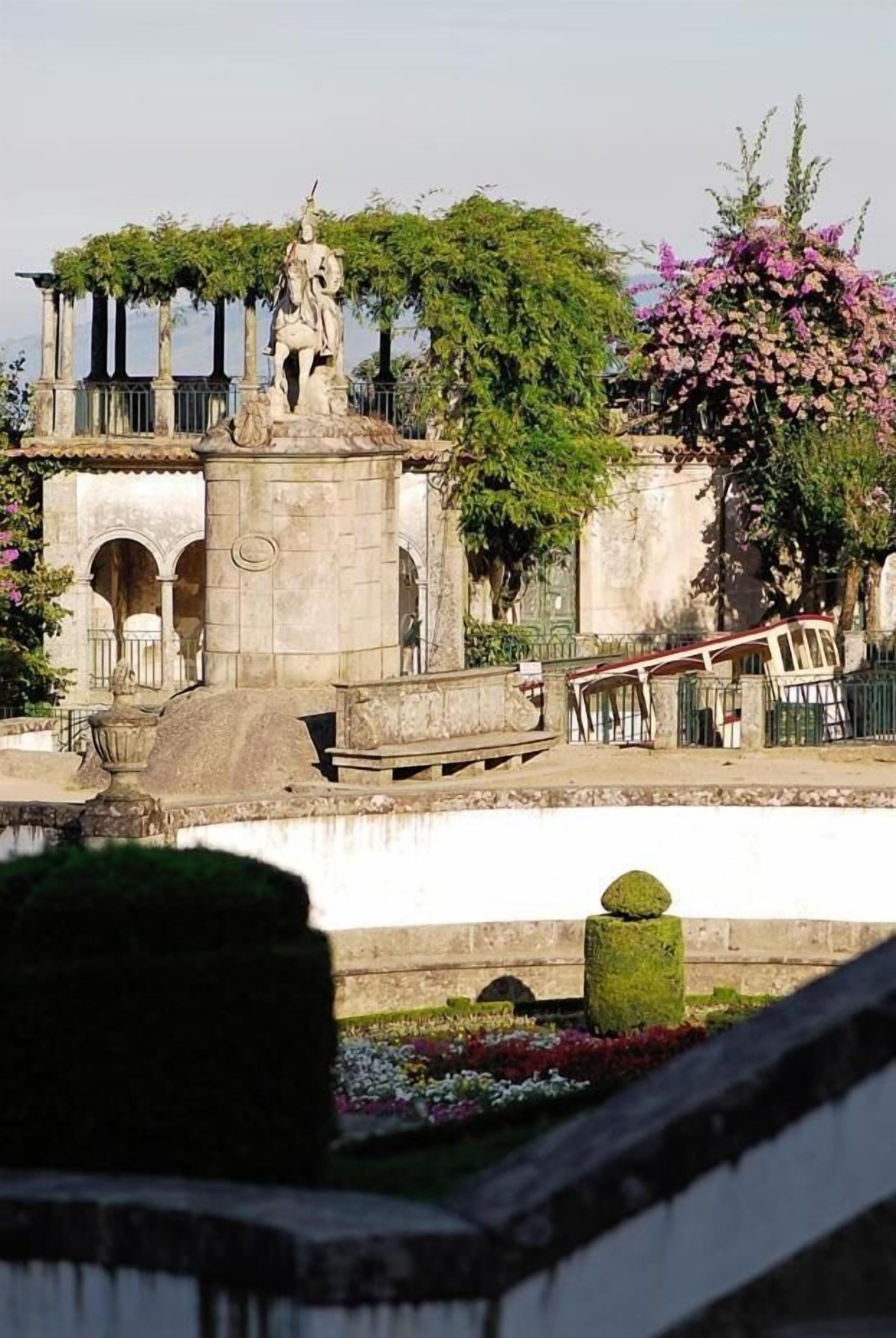 A historical monument with a statue, surrounded by greenery and a fountain.