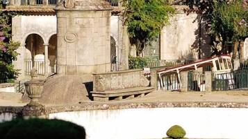 A historical monument with a statue, surrounded by greenery and a fountain.