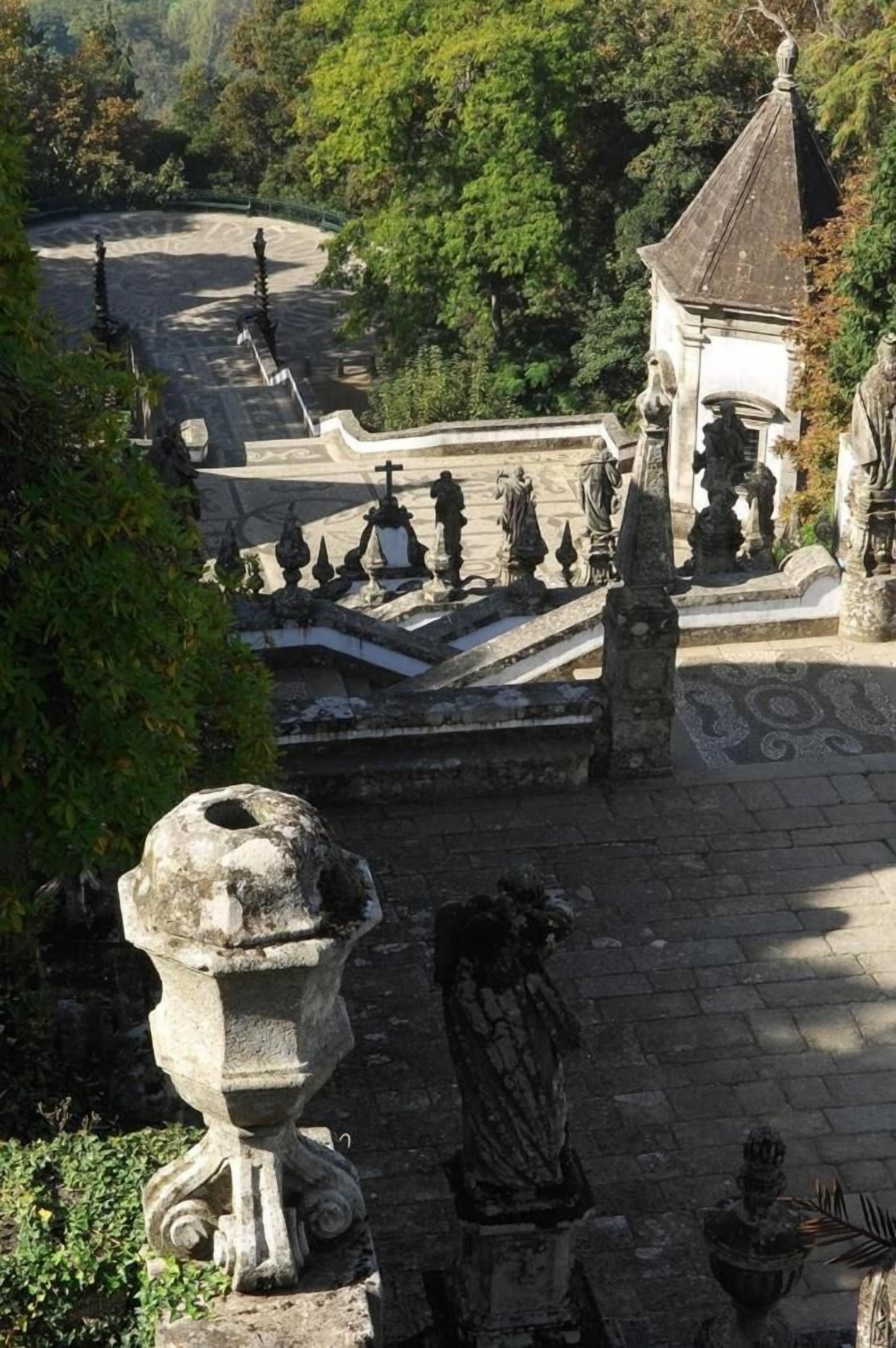 A stone pathway leading to a gazebo surrounded by statues and a large urn.