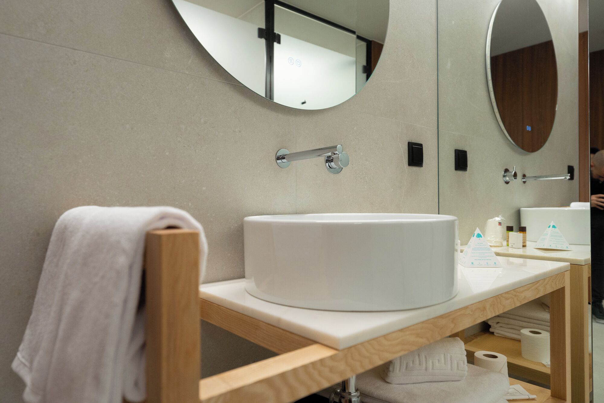 A modern bathroom with a round sink, a mirror, and a towel rack.