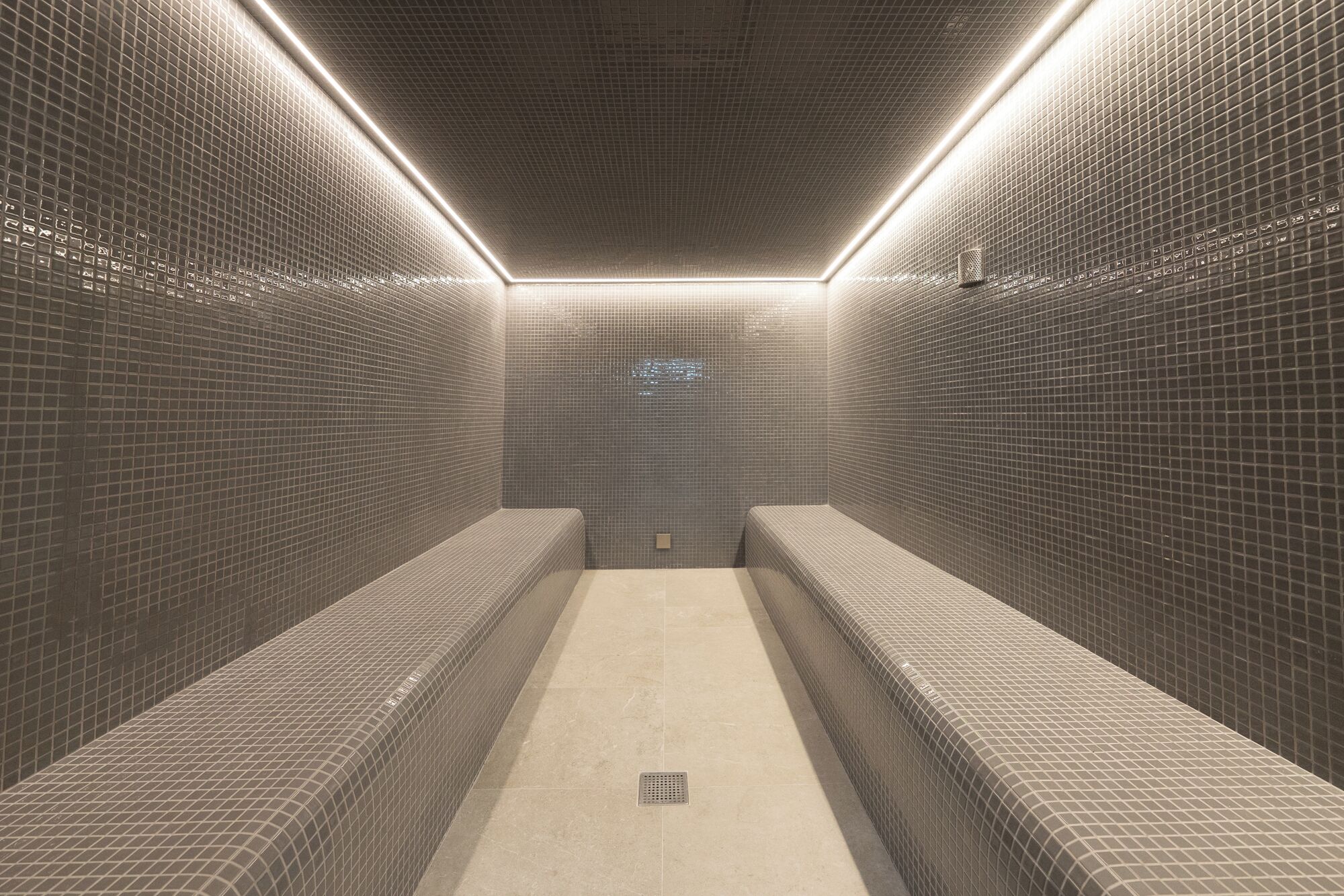 Une salle de bain carrelée, avec des bancs et un drain au centre.