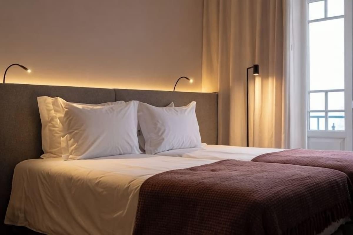 Une chambre d’hôtel avec un lit, deux lampes de chevet, une fenêtre avec des rideaux et une vue sur l’extérieur.