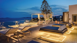 A rooftop lounge area with sun loungers, a large tree, and a view of the sea. - Grace Mykonos (Mykonos)