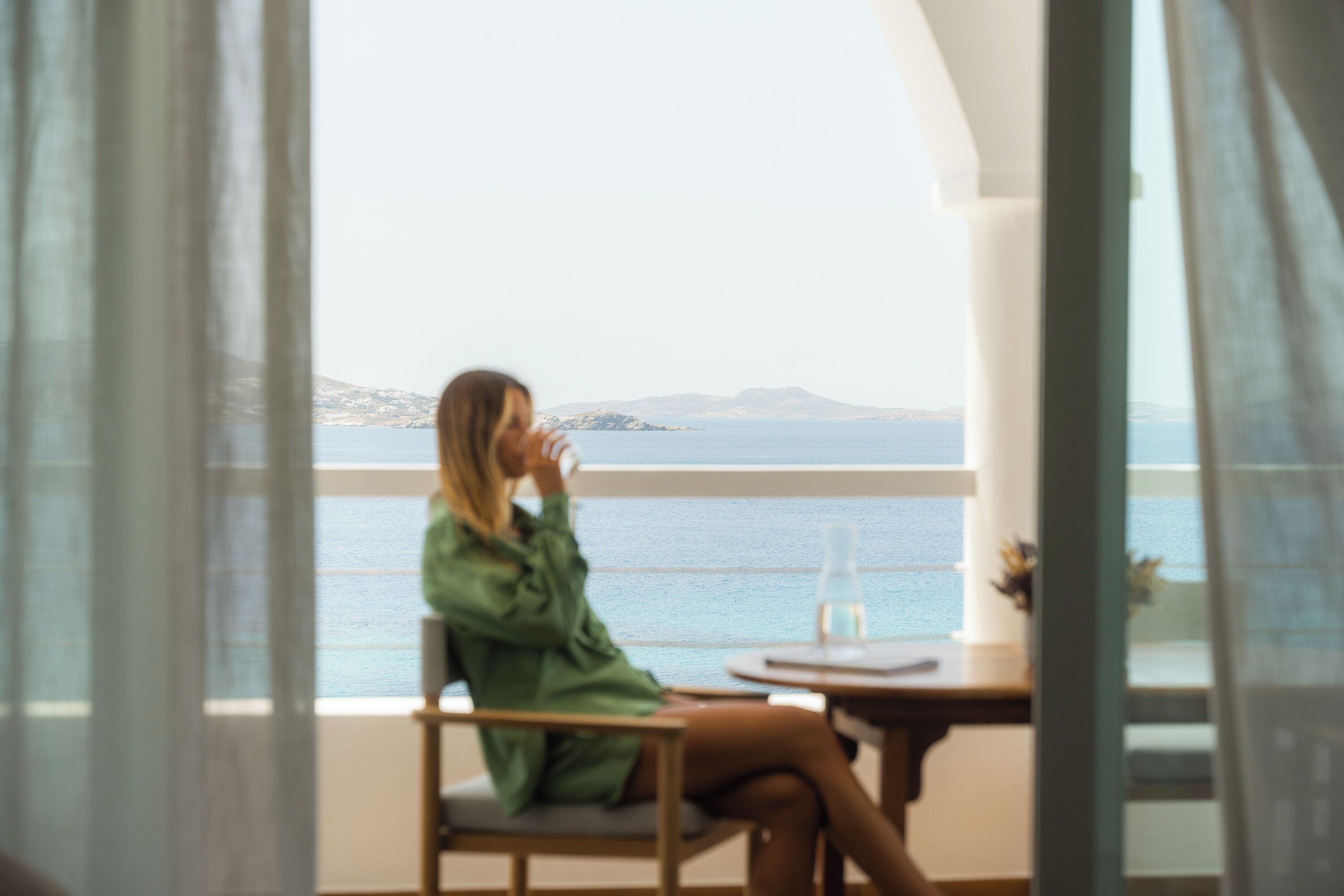 A person sitting by a window overlooking a body of water with distant landforms.